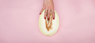 Hands with red fingernails on melon that resembles a vulva