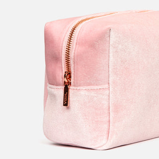 Close up of side of pink soft cosmetics bag made of fuzzy velvet-like material with rose gold zipper against light grey background