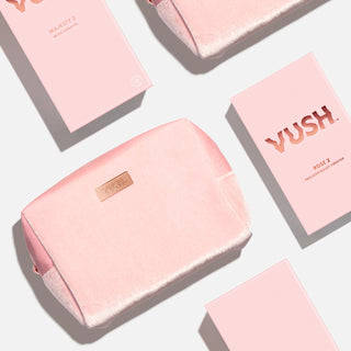 Pink soft cosmetics bag made of fuzzy velvet-like material with rose gold plaque that reads "VUSH" lying flat next to pink rectangular box that reads "VUSH ROSE 2 PRECISION BULLET VIBRATOR" against light grey background