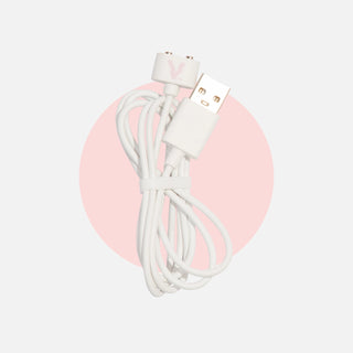 White cord with magnetic charging point with pink 'V' on head on one end and USB adapter on other end, against light grey background with pink filled circle around product