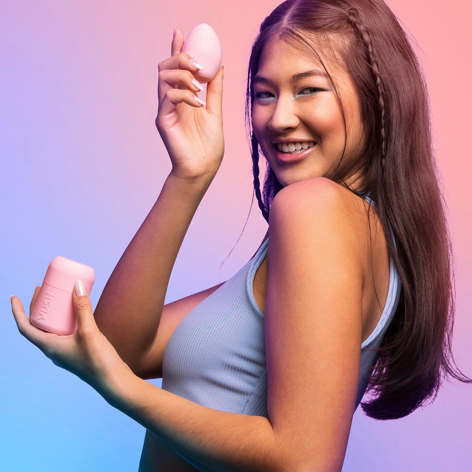Young woman wearing blue tank top smiling, holding VUSH Plump Palm Vibrator up in right hand and case in left hand.
