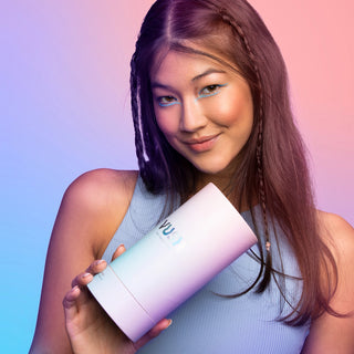 Young woman with long dark hair smiling and wearing a baby blue tank top while holding blue/purple/pink gradient cylinder packaging that reads "VUSH"